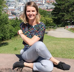 Person auf kleiner Mauer vor Stadtausblick mit überkreuzten Beinen